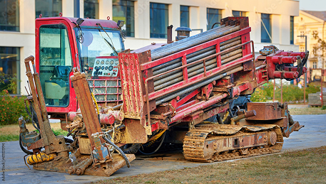 A red horizontal directional drilling machine with tank tracks is parked on grass